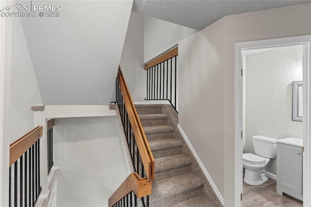 stairway featuring a textured ceiling, wood finished floors, and baseboards
