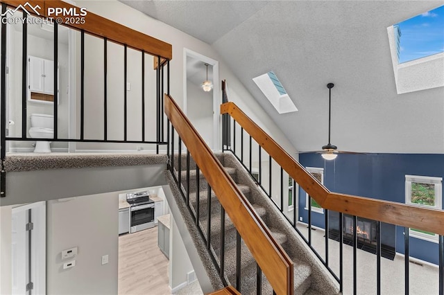 stairs with a skylight, lofted ceiling, a textured ceiling, ceiling fan, and wood finished floors