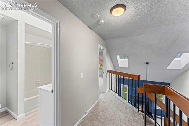 hall with a skylight, a textured ceiling, baseboards, an upstairs landing, and healthy amount of natural light