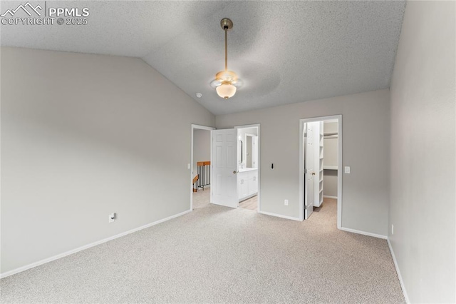 unfurnished bedroom with a spacious closet, light colored carpet, vaulted ceiling, baseboards, and ceiling fan