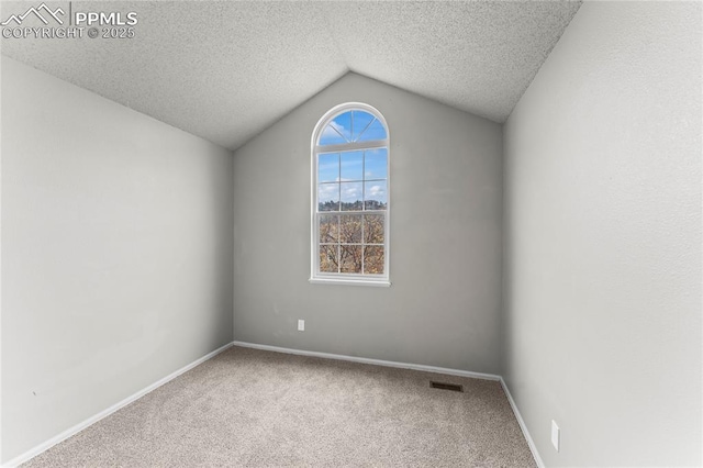 carpeted spare room with vaulted ceiling, a textured ceiling, and baseboards