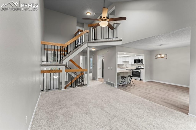 living room with light carpet, baseboards, ceiling fan, stairs, and a high ceiling
