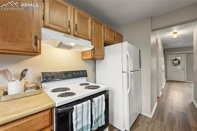 kitchen featuring electric range oven, under cabinet range hood, freestanding refrigerator, and wood finished floors