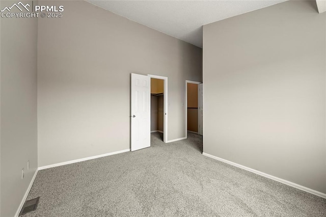 unfurnished bedroom with carpet flooring, baseboards, a high ceiling, and a spacious closet