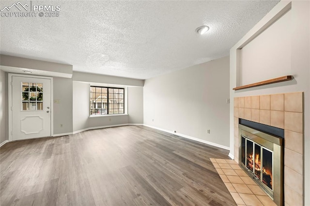 unfurnished living room with a textured ceiling, a tile fireplace, wood finished floors, and baseboards