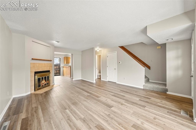 unfurnished living room featuring a textured ceiling, light wood finished floors, a tile fireplace, baseboards, and stairway