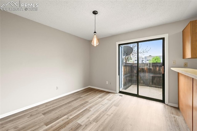 unfurnished dining area with light wood-style floors, baseboards, and a textured ceiling