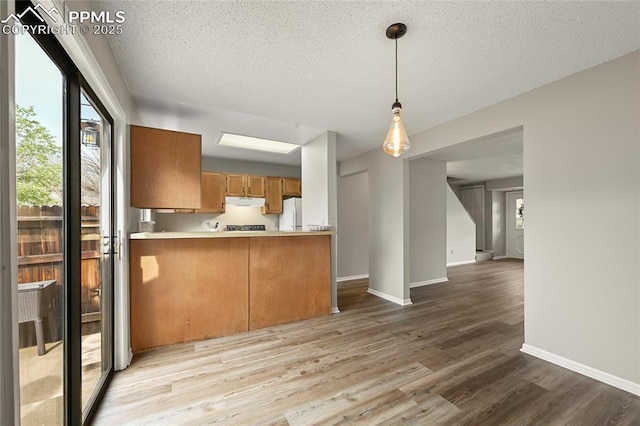 kitchen featuring wood finished floors, under cabinet range hood, baseboards, freestanding refrigerator, and a textured ceiling
