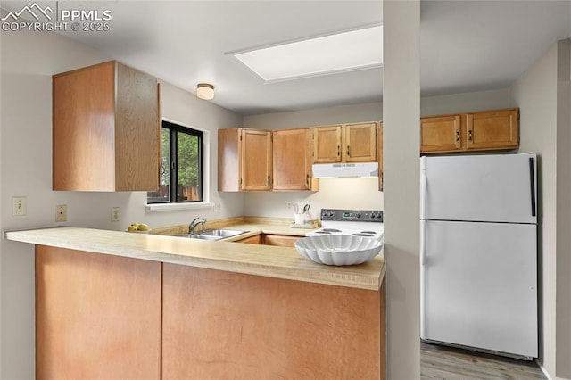 kitchen with freestanding refrigerator, electric range oven, a sink, light countertops, and a peninsula