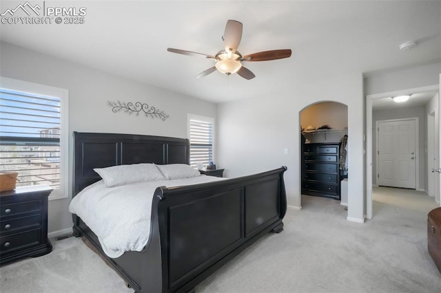 bedroom featuring light carpet, a spacious closet, baseboards, arched walkways, and a ceiling fan