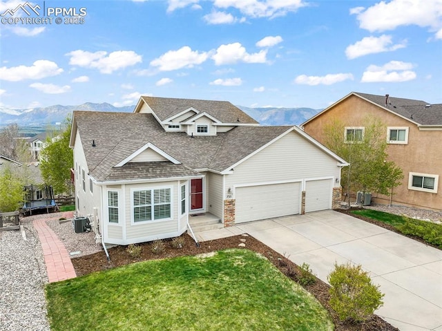 traditional-style home with a shingled roof, an attached garage, concrete driveway, a mountain view, and central air condition unit