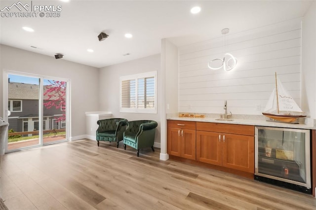 indoor wet bar with beverage cooler, light wood finished floors, recessed lighting, baseboards, and hanging light fixtures