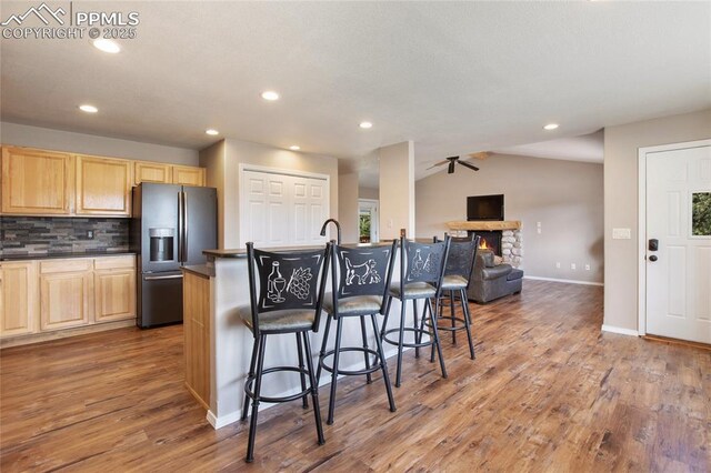 kitchen featuring fridge with ice dispenser, dark countertops, light brown cabinetry, wood finished floors, and lofted ceiling