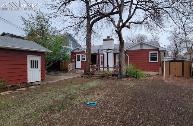 back of property with an outbuilding, a chimney, a shed, and fence