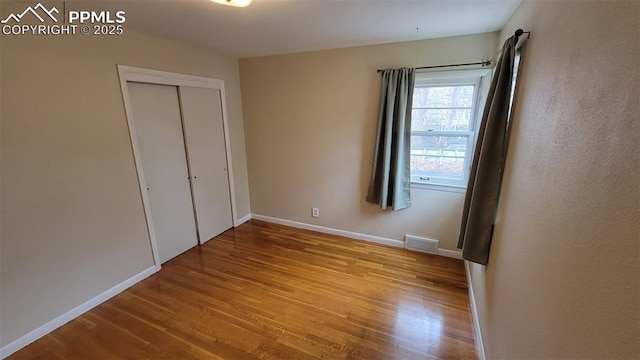 unfurnished bedroom with wood finished floors, baseboards, and a closet