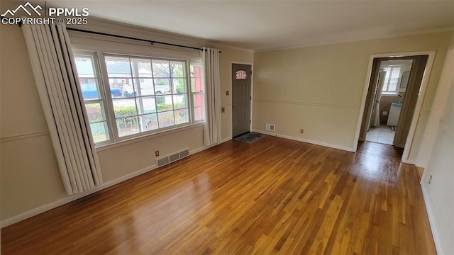 empty room with wood finished floors, healthy amount of natural light, ornamental molding, and baseboards