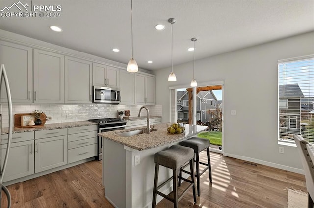 kitchen with appliances with stainless steel finishes, a sink, decorative backsplash, wood finished floors, and healthy amount of natural light