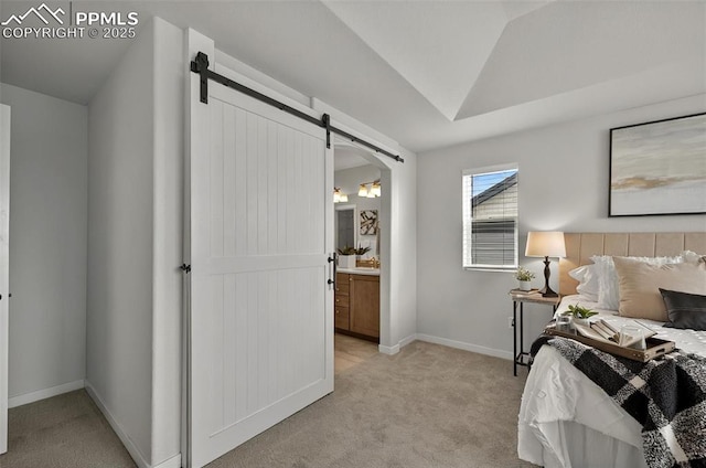 bedroom with light colored carpet, a barn door, ensuite bath, and baseboards