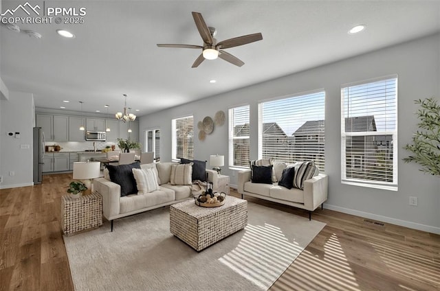 living room with light wood-type flooring, recessed lighting, ceiling fan, baseboards, and a chandelier