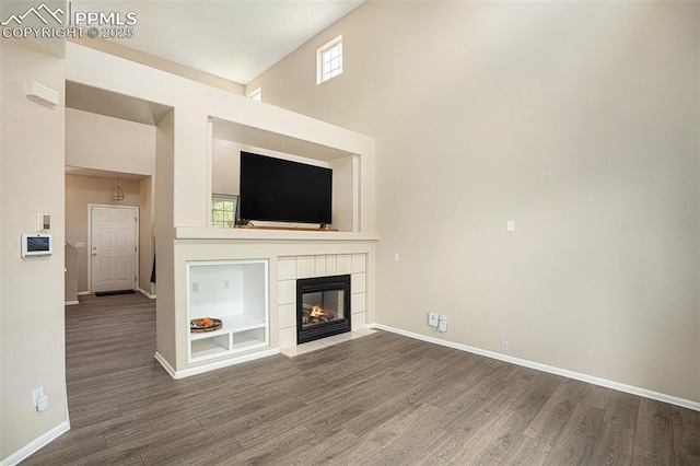 7120 Bonnie Brae Ln, Colorado Springs, CO 80922 - unfurnished living room featuring wood finished floors, built in features, baseboards, a tile fireplace, and a towering ceiling