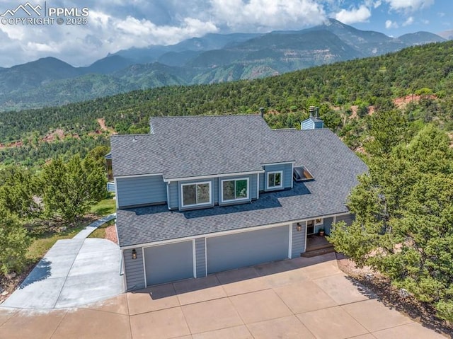 2530 White Rock Ln, Colorado Springs, CO 80904 - view of front facade with a wooded view, a shingled roof, driveway, a mountain view, and a garage