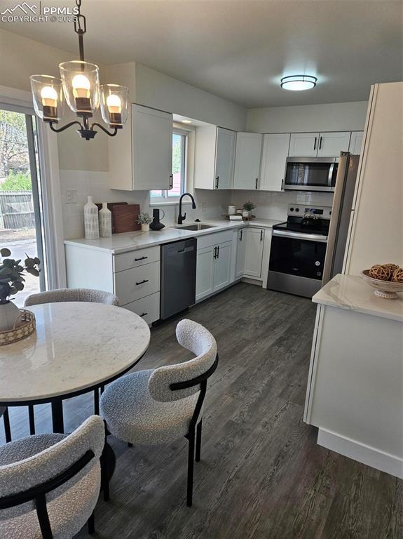 910 Dunston St, Colorado Springs, CO 80907 - kitchen with stainless steel appliances, a sink, a chandelier, dark wood-style floors, and white cabinets