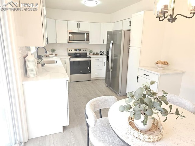 910 Dunston St, Colorado Springs, CO 80907 - kitchen featuring stainless steel appliances, a sink, light wood-style floors, white cabinetry, and decorative backsplash