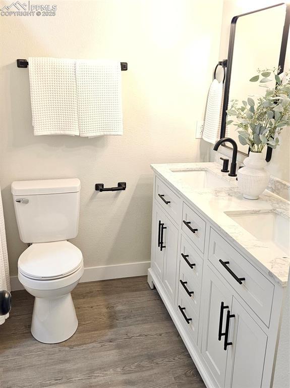 910 Dunston St, Colorado Springs, CO 80907 - bathroom featuring baseboards, wood finished floors, toilet, and double vanity