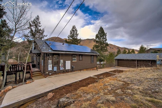 back of house with log veneer siding, roof mounted solar panels, a detached garage, an outdoor structure, and a deck with mountain view
