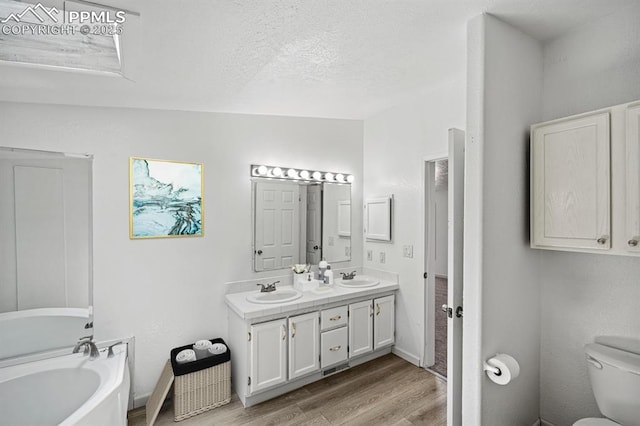 9775 Indian Village Hts, Fountain, CO 80817 - full bathroom featuring wood finished floors, a bath, toilet, double vanity, and a textured ceiling