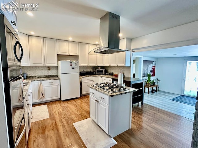 1701 Jerry Murphy Rd, Pueblo, CO 81001 - kitchen with freestanding refrigerator, island exhaust hood, stainless steel gas cooktop, decorative backsplash, and light wood-style flooring