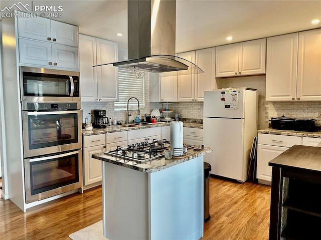 1701 Jerry Murphy Rd, Pueblo, CO 81001 - kitchen with appliances with stainless steel finishes, island range hood, tasteful backsplash, white cabinetry, and light wood-style floors