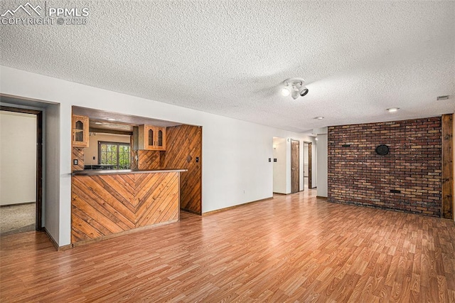 7210 Antelope Ln, Colorado Springs, CO 80920 - unfurnished living room featuring light wood-style flooring, brick wall, a textured ceiling, bar area, and baseboards