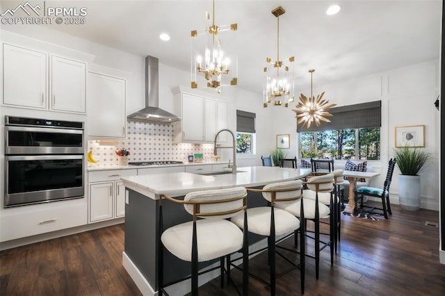 kitchen with wall chimney exhaust hood, a sink, a chandelier, gas stovetop, and light countertops