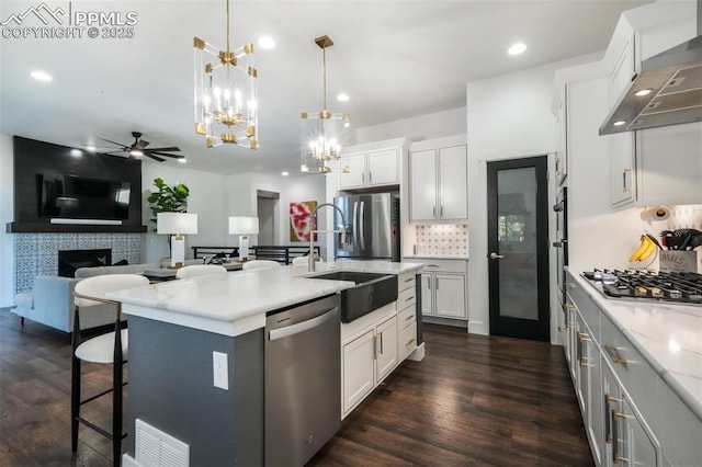 kitchen featuring appliances with stainless steel finishes, wall chimney range hood, a sink, a chandelier, and backsplash