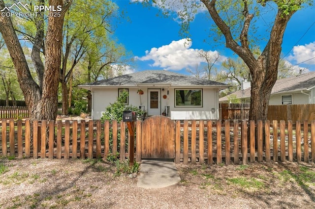 bungalow-style house with a fenced front yard, stucco siding, and a gate