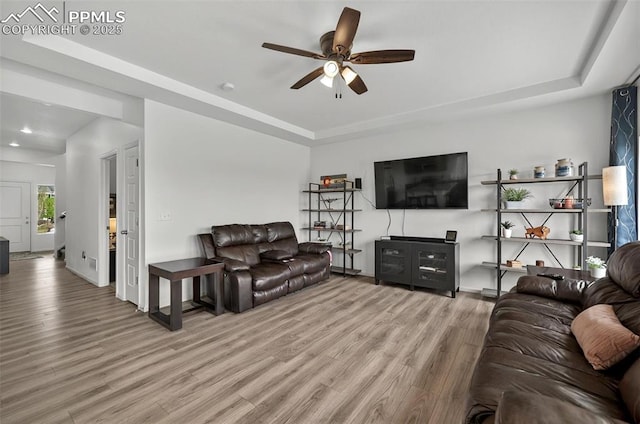 living area featuring a raised ceiling, wood finished floors, ceiling fan, recessed lighting, and baseboards