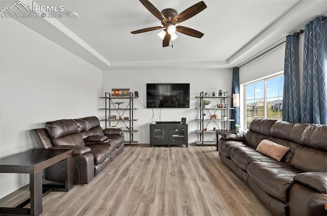 living room featuring a tray ceiling, ceiling fan, light wood-type flooring, and baseboards