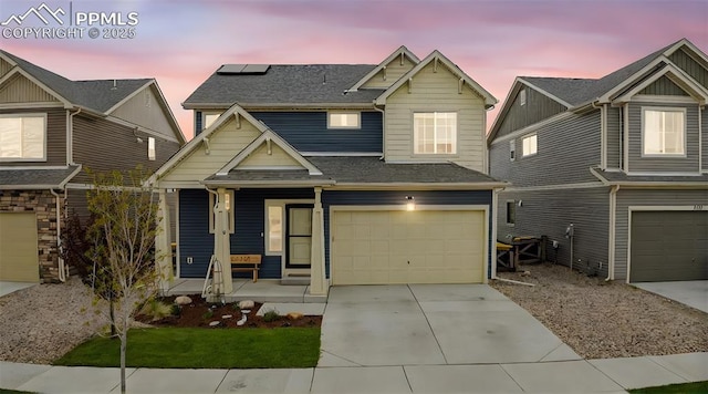 craftsman-style home featuring a porch, a garage, a shingled roof, concrete driveway, and solar panels