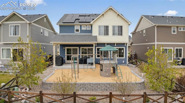 rear view of house featuring a patio, roof mounted solar panels, a fenced backyard, and a shingled roof