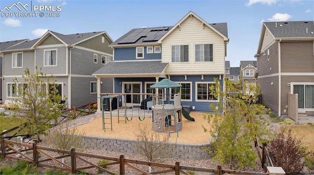 rear view of house with roof mounted solar panels, a fenced backyard, a patio, a shingled roof, and a residential view