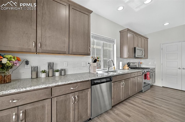 kitchen featuring stainless steel appliances, a sink, light wood-type flooring, light stone counters, and recessed lighting