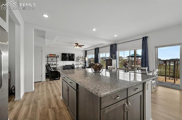 kitchen with recessed lighting, a raised ceiling, light wood-type flooring, light stone countertops, and open floor plan
