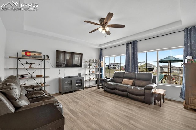 living room featuring a raised ceiling, a ceiling fan, and healthy amount of natural light