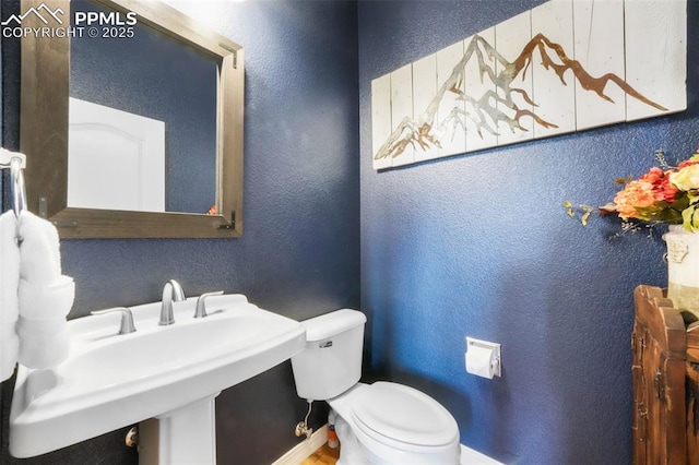 half bathroom featuring a textured wall, toilet, and a sink