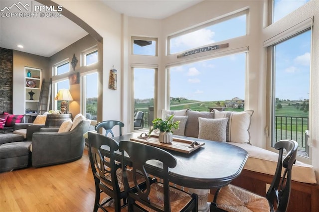 dining room featuring arched walkways, light wood-style floors, and a high ceiling