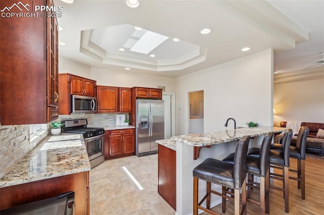 2744 La Strada Grande Hts, Colorado Springs, CO 80906 - kitchen with stainless steel appliances, a peninsula, a kitchen breakfast bar, decorative backsplash, and light stone counters