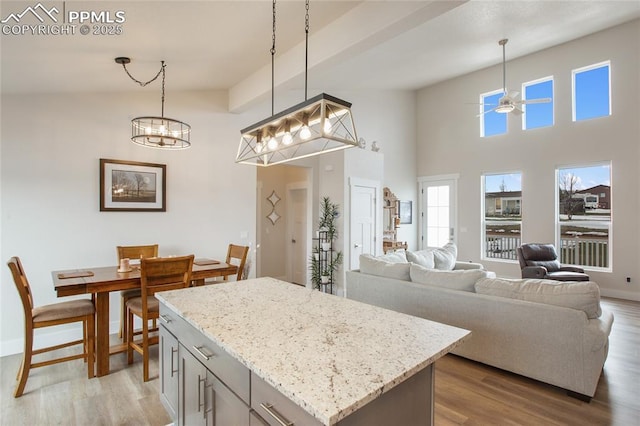 kitchen with light wood-style flooring, a ceiling fan, pendant lighting, light stone counters, and a high ceiling