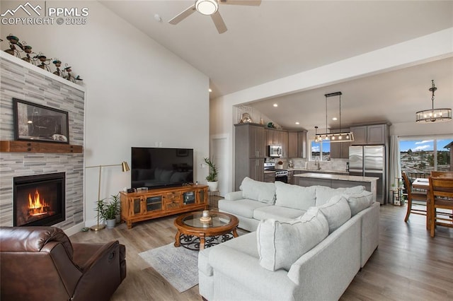 living area featuring a fireplace, light wood-style flooring, ceiling fan, high vaulted ceiling, and recessed lighting