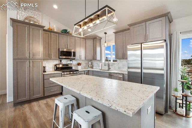 kitchen with stainless steel appliances, a sink, light wood finished floors, decorative backsplash, and lofted ceiling